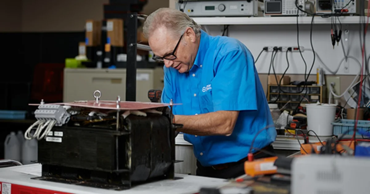 Technician in a blue shirt working on electronic equipment in a repair lab.